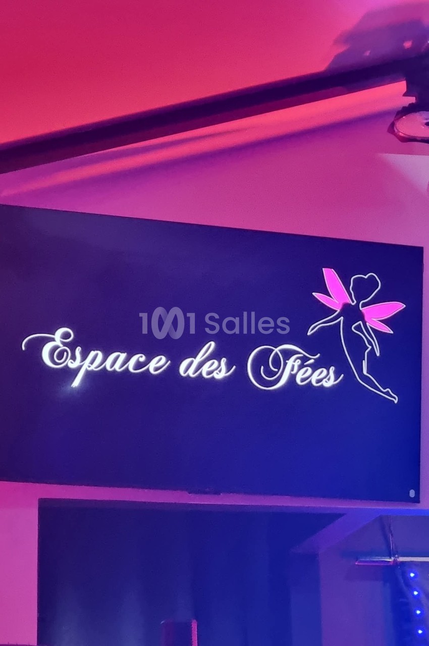 Enseigne lumineuse néon blanc et rose sur fond bleu dans une salle éclairée en rose et violet.