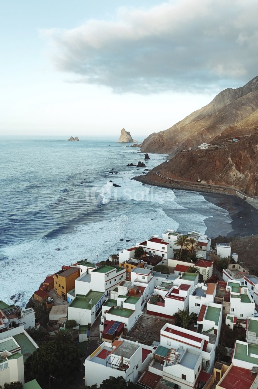 Village côtier avec maisons blanches et toits colorés surplombant une plage et des rochers en mer.