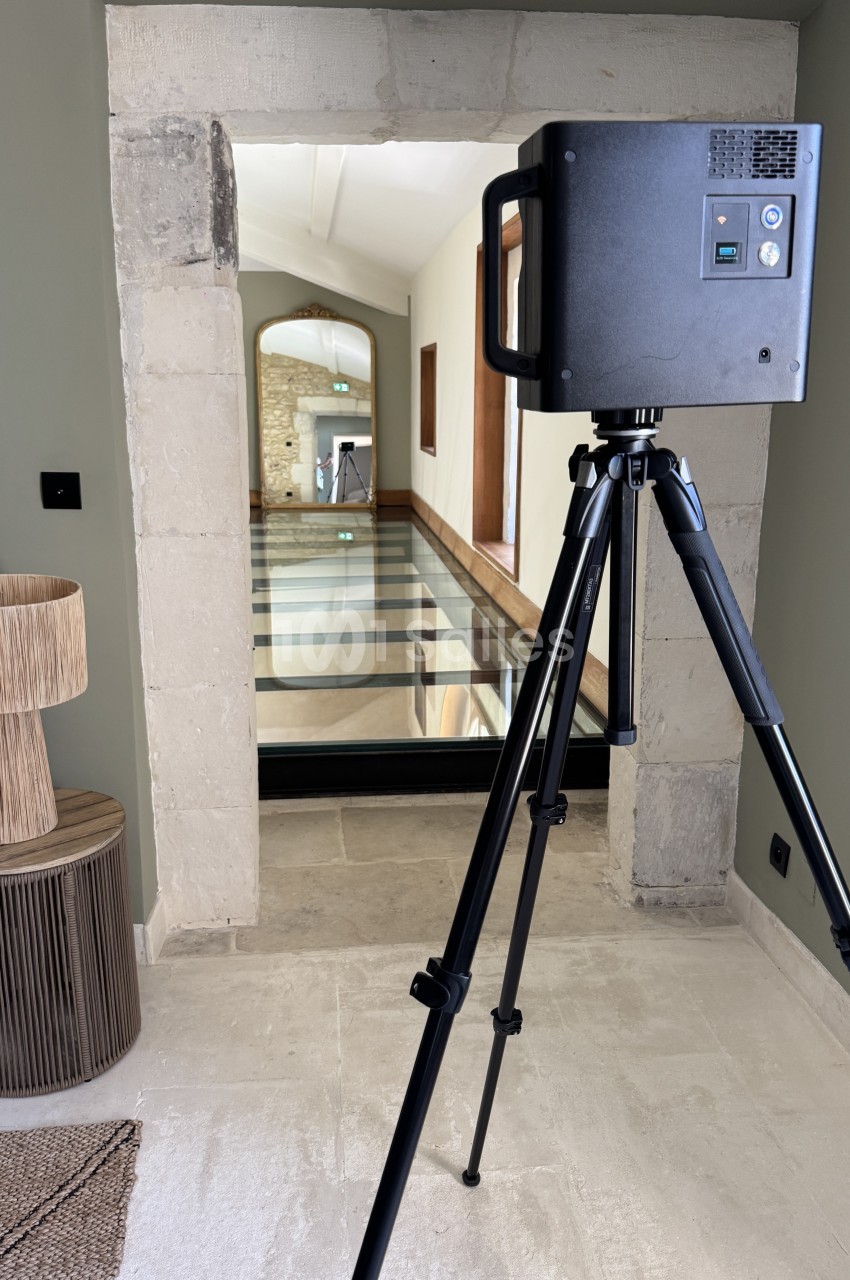 Scanner 3D positionné sur trépied dans un couloir, capturant l'intérieur d'un bâtiment.