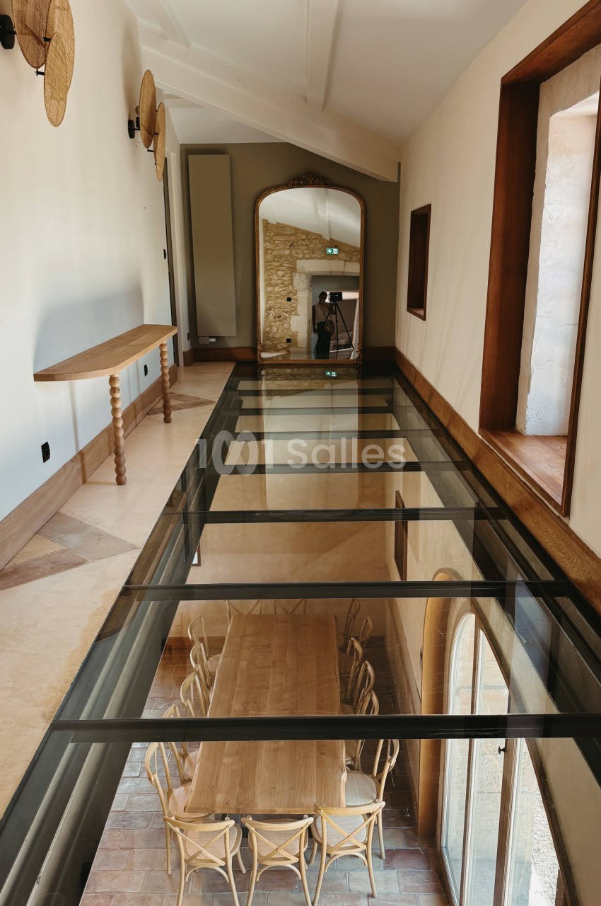 Couloir intérieur avec sol en marbre, miroir encadré et tables basses en verre révélant des chaises en rotin à l'étage inférieur.
