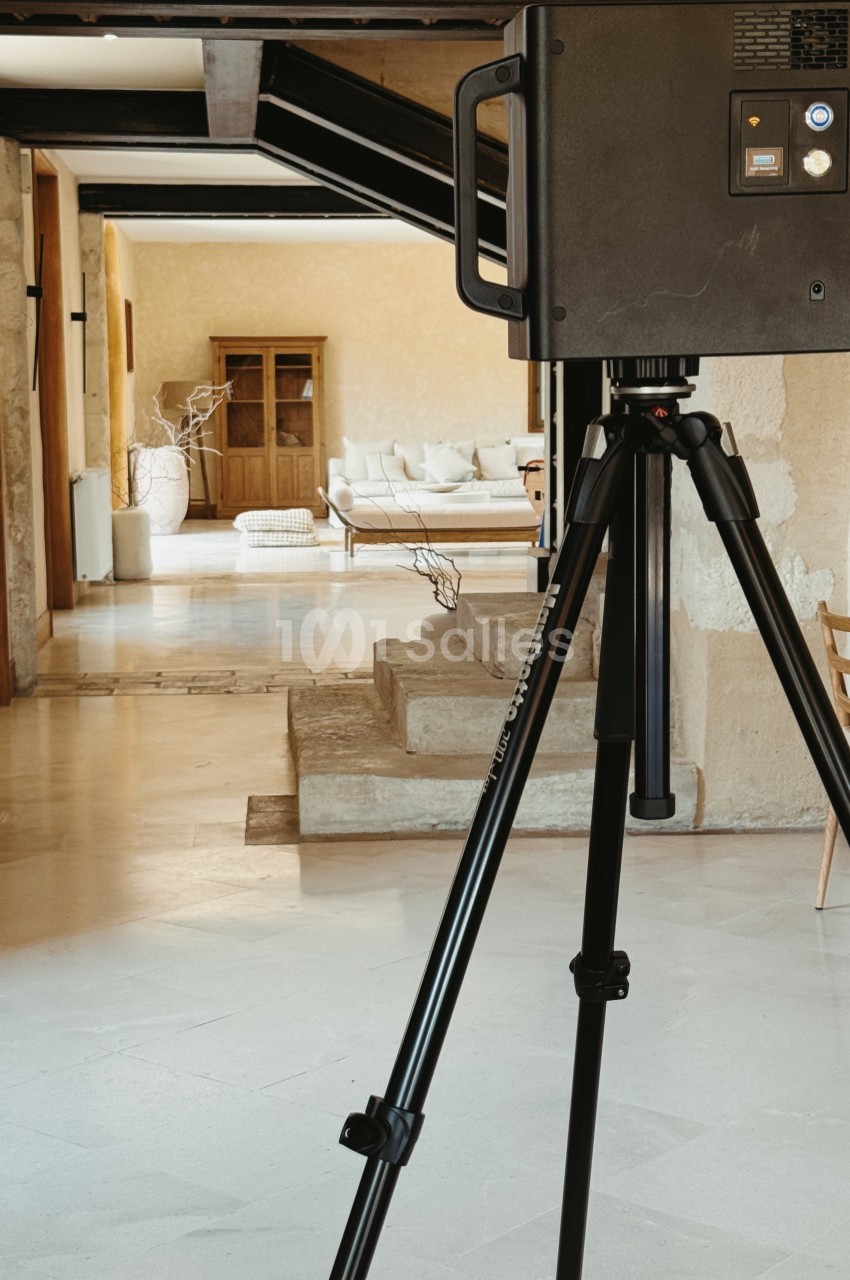 Caméra professionnelle sur trépied filmant un loft moderne au sol clair avec canapé beige et portes bois.