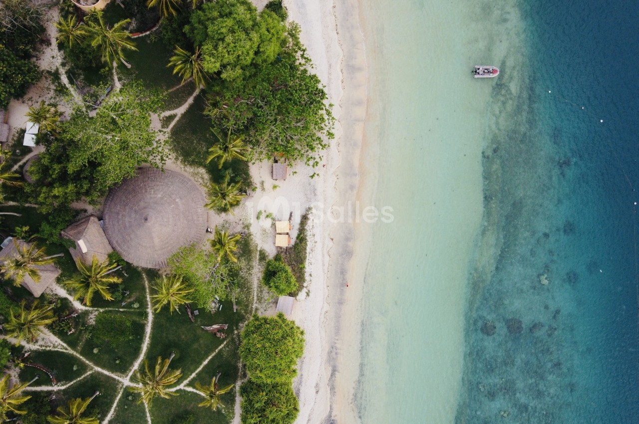 Vue aérienne d'une plage tropicale avec végétation dense, structure circulaire et lagon turquoise.