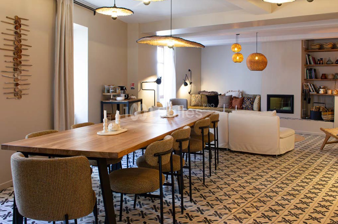 Salle intérieure avec table en bois massif, chaises en tissu, canapés beige et luminaires dorés suspendus.