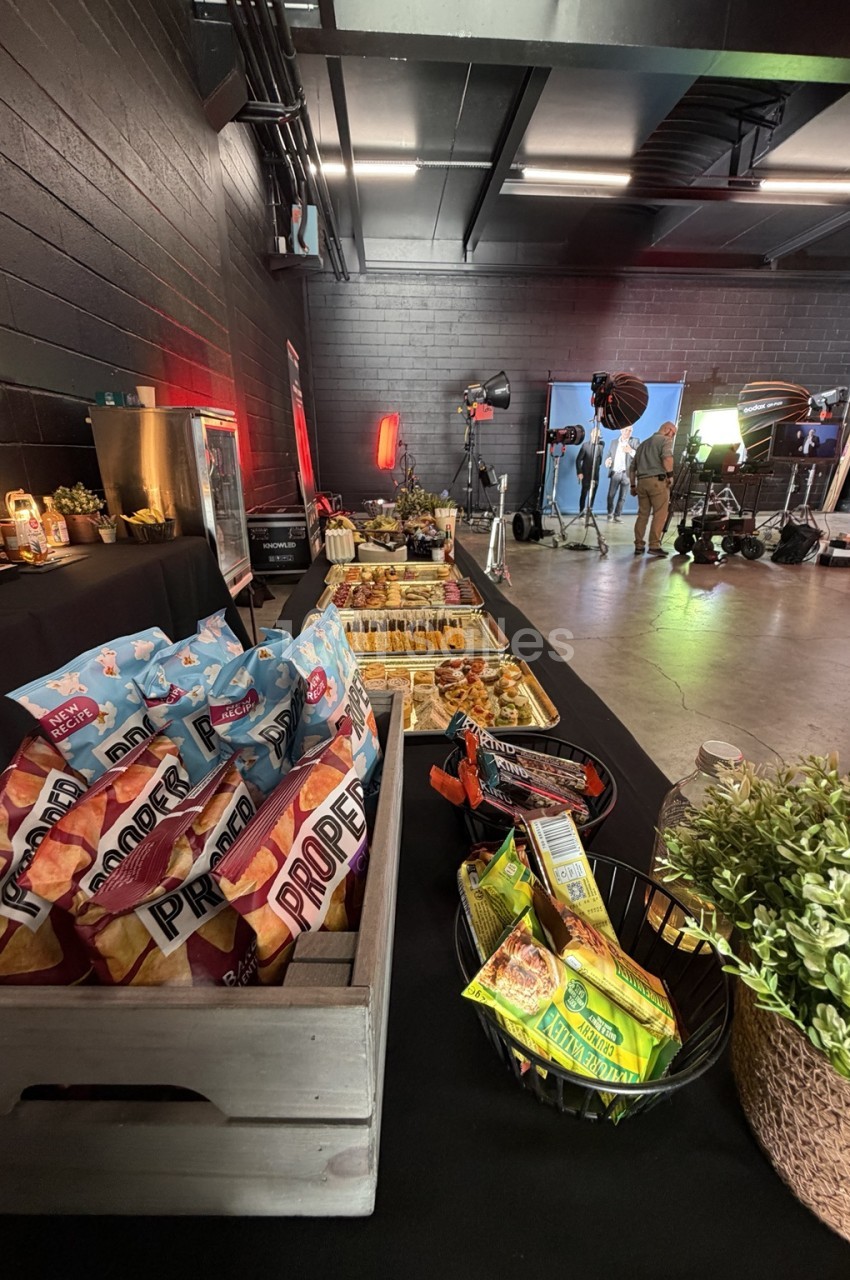Buffet de canapés et de snacks dans une salle en brique noire, avec un plateau de tournage en arrière-plan.