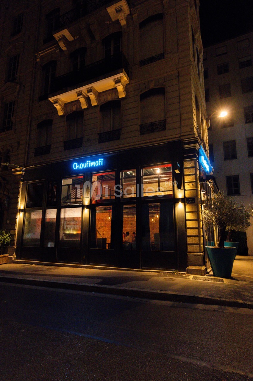 Façade vitrée de restaurant illuminée la nuit, enseigne bleue Choufimafi, bâtiment haussmannien en pierre à l'arrière-plan.