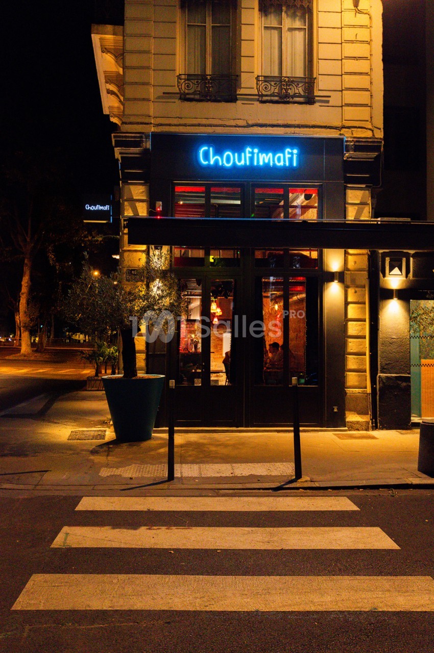 Façade de restaurant de nuit avec enseigne lumineuse bleue, immeuble haussmannien beige à l'étage.