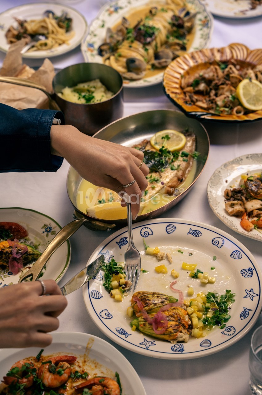 Table dressée avec fruits de mer, pâtes et poissons garnis de citron et persil - convives en train de manger.