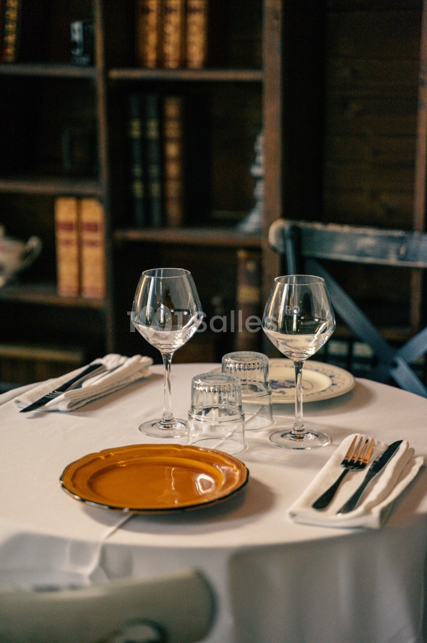 Table dressée avec assiette orange, verres à vin et couverts sur nappe blanche - décor intérieur sobre.
