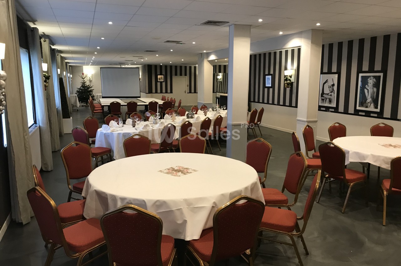 Salle de réception dressée de tables rondes nappées de blanc avec chaises rouges, murs rayés noir et blanc et grand écran de projection au fond.