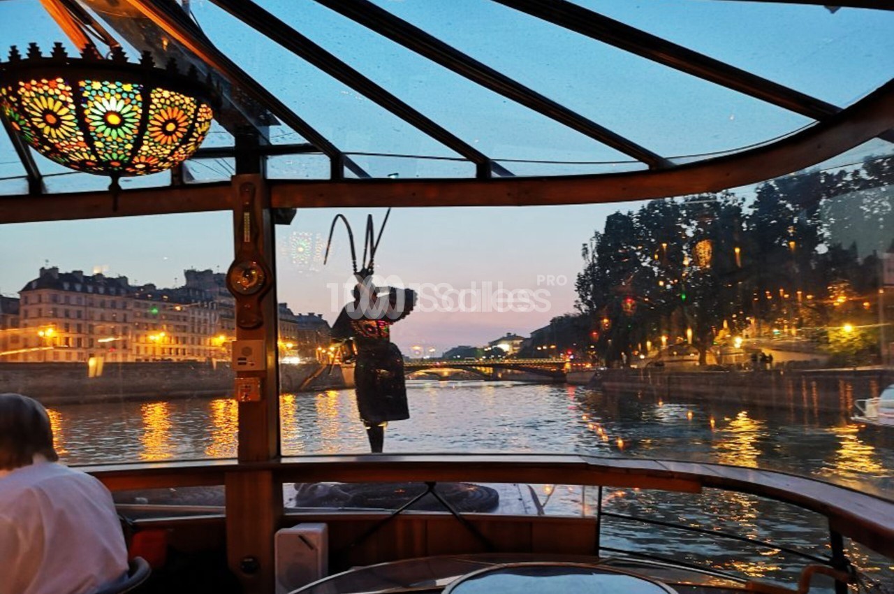 Intérieur d'un bateau vitré au crépuscule sur la Seine, avec lustre en verre coloré et vue sur les quais éclairés.