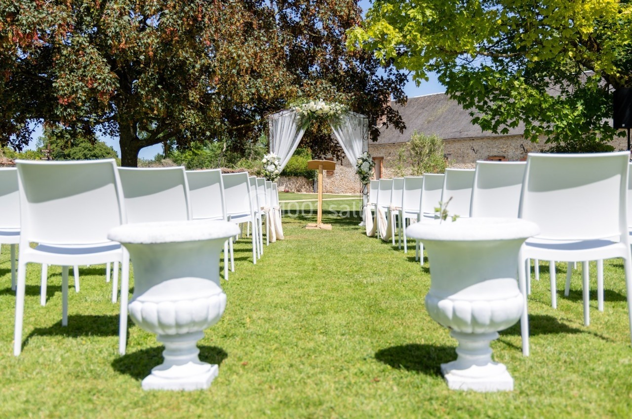 Allée centrale d'une cérémonie en plein air, bordée de chaises blanches et décorée d'une arche florale.