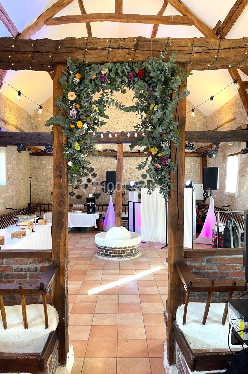Salle de réception rustique avec poutres apparentes, décor floral suspendu et éclairage festif.