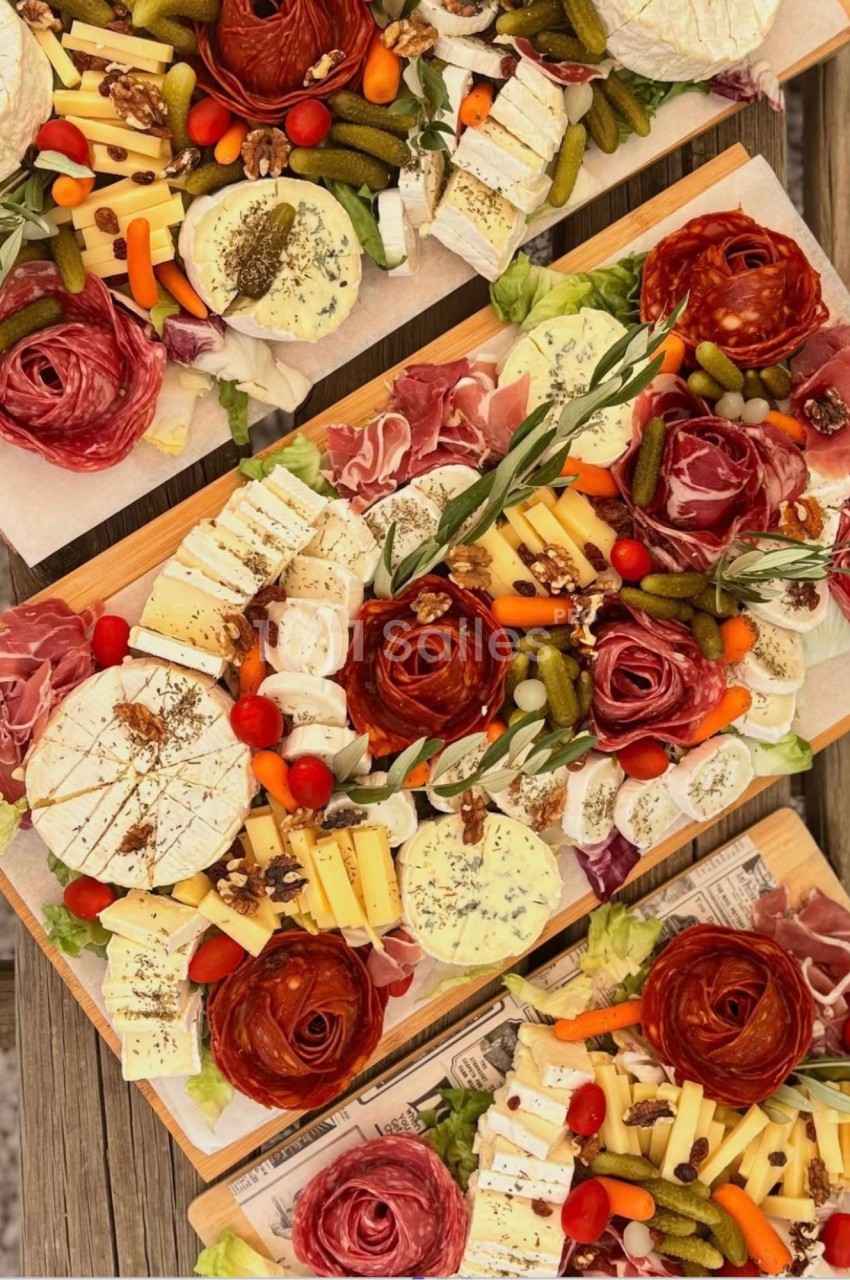 Planches en bois garnies de roses de saucisson, fromages à pâte molle, cornichons, tomates cerises et carottes.