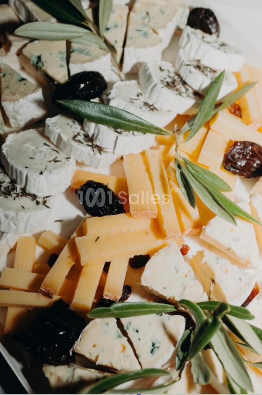 Plateau de fromages variés : tranches de bûche à croûte fleurie garnie de thym, cubes de bleu, pavés de fromage à pâte dure et prunes séchées, décorés de branches d'olivier. Let me check length: roughly 165 characters, too long. Need ≤125. Plateau de