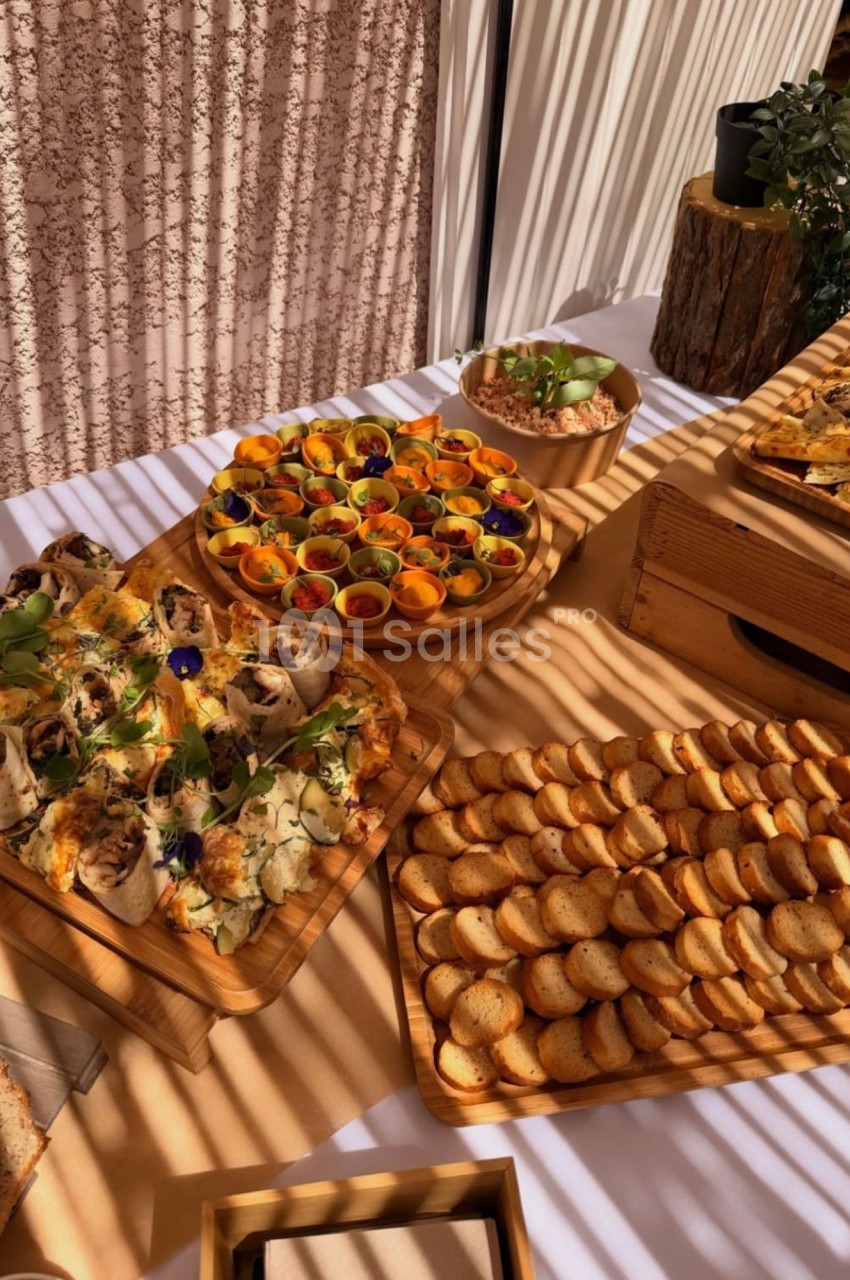 Buffet de petites bouchées sur plateaux en bois : roulés, tartes salées, toasts ronds et coupelles colorées garnies, sous une lumière chaude.