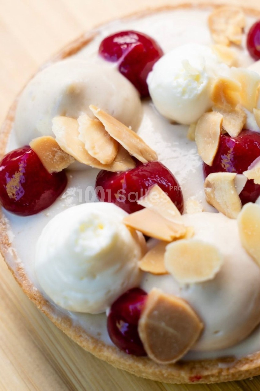 Tartelette garnie de crème blanche, de cerises rouges brillantes, de boules de glace vanille et d'amandes effilées dorées, en gros plan.
