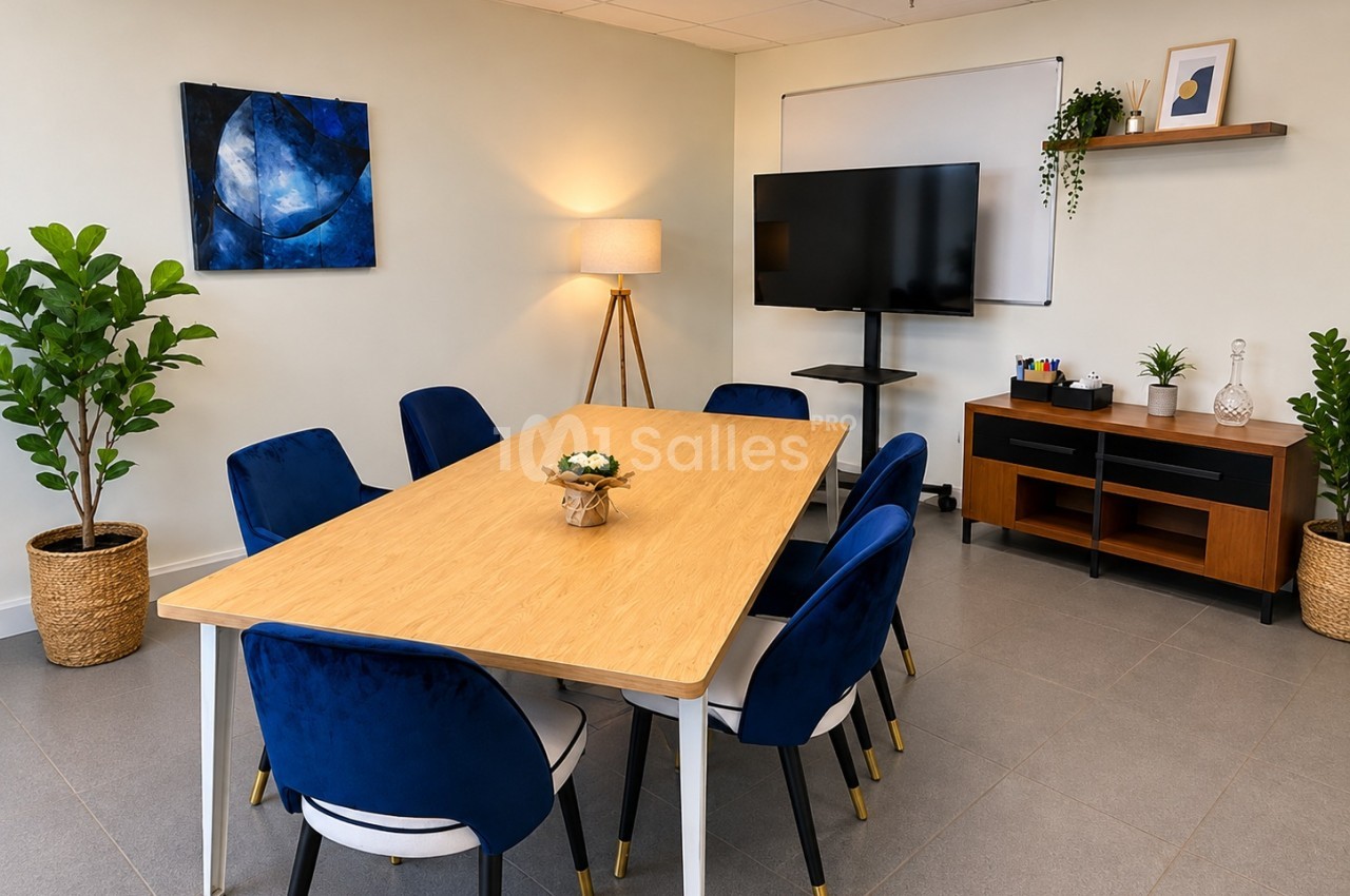 Salle de réunion avec une grande table en bois entourée de six chaises bleues, un écran TV sur pied, un tableau blanc et une plante verte. Let me check length: roughly 150 characters - too long. Need ≤125. Salle de réunion avec une table en bois entourée