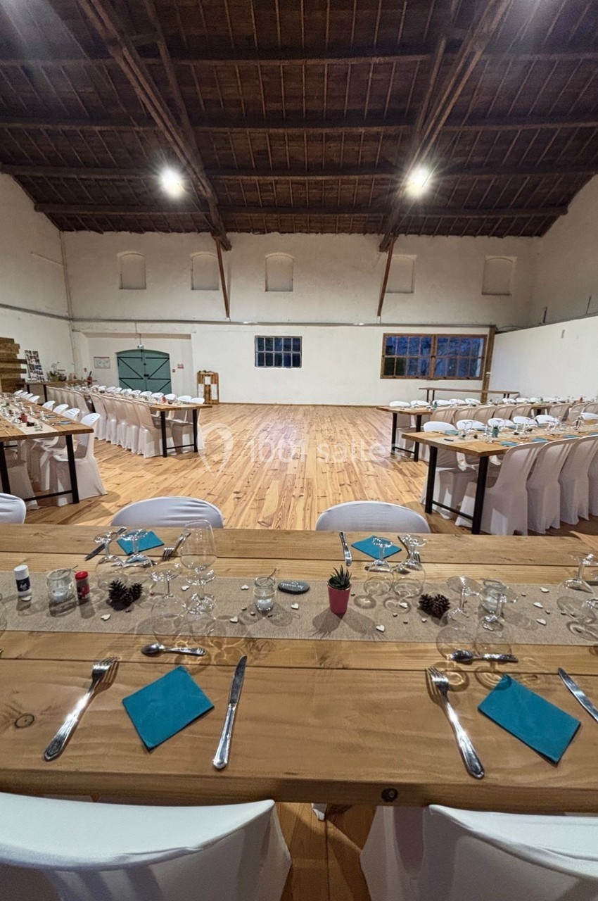 Salle de réception décorée avec des tables dressées, nappes blanches, chemins de table et serviettes bleues.