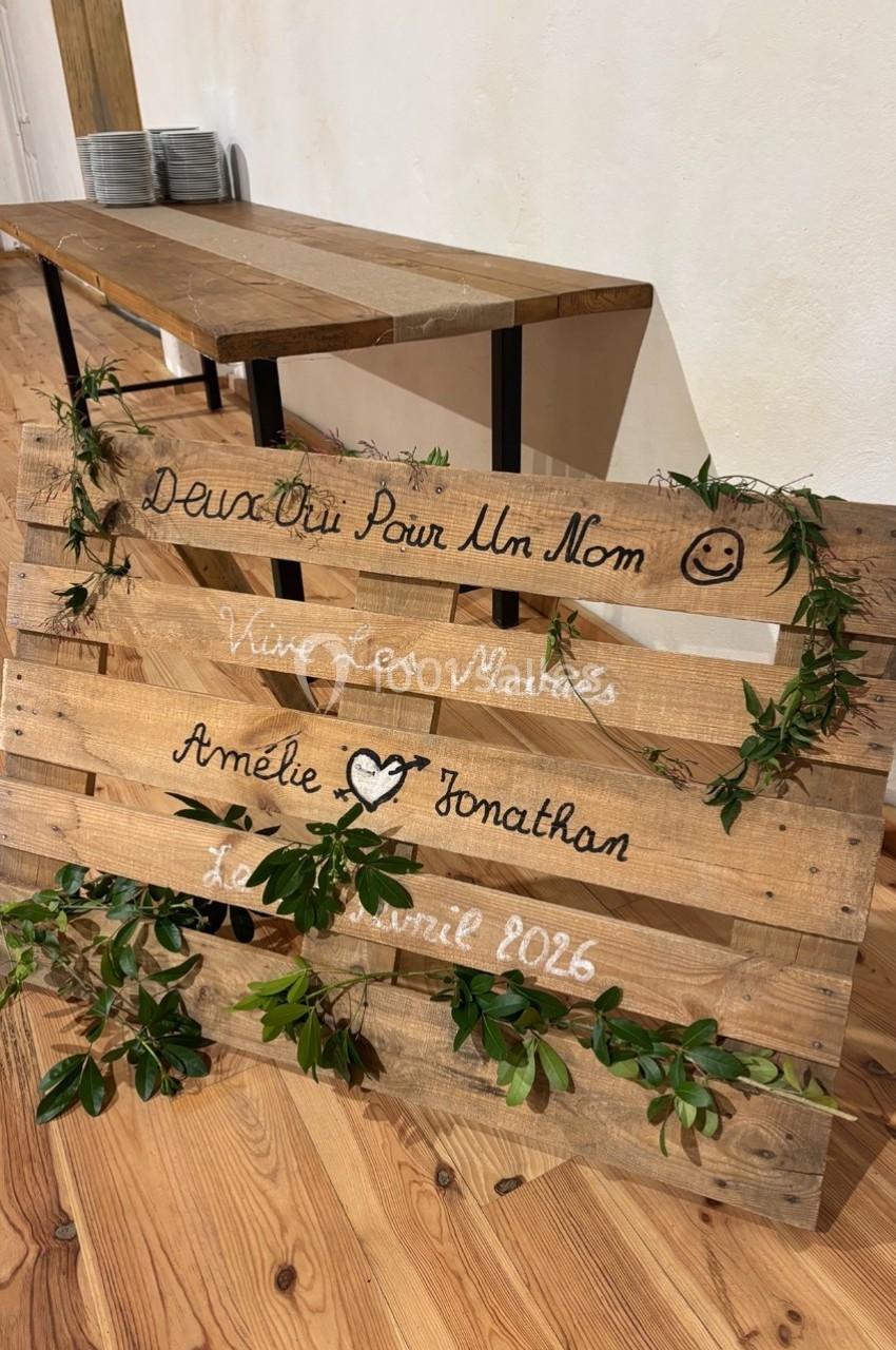 Palette en bois décorée de feuillage, avec des inscriptions manuscrites annonçant un mariage en avril 2026.