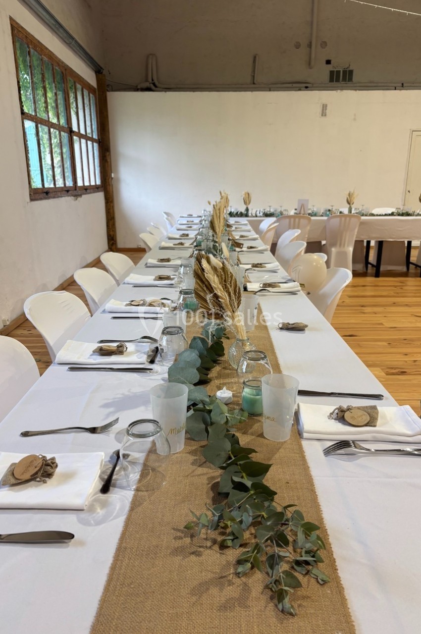 Grande table de réception décorée avec un chemin de table en toile de jute, des feuillages et des ornements naturels.