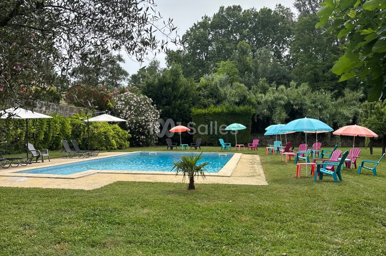Piscine extérieure entourée de chaises colorées, parasols et végétation dense dans un jardin.
