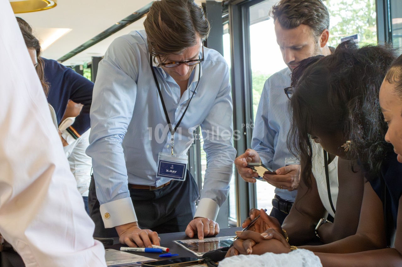 Groupe réuni autour d'une table, un homme penché sur des documents et d'autres consultant leur téléphone.