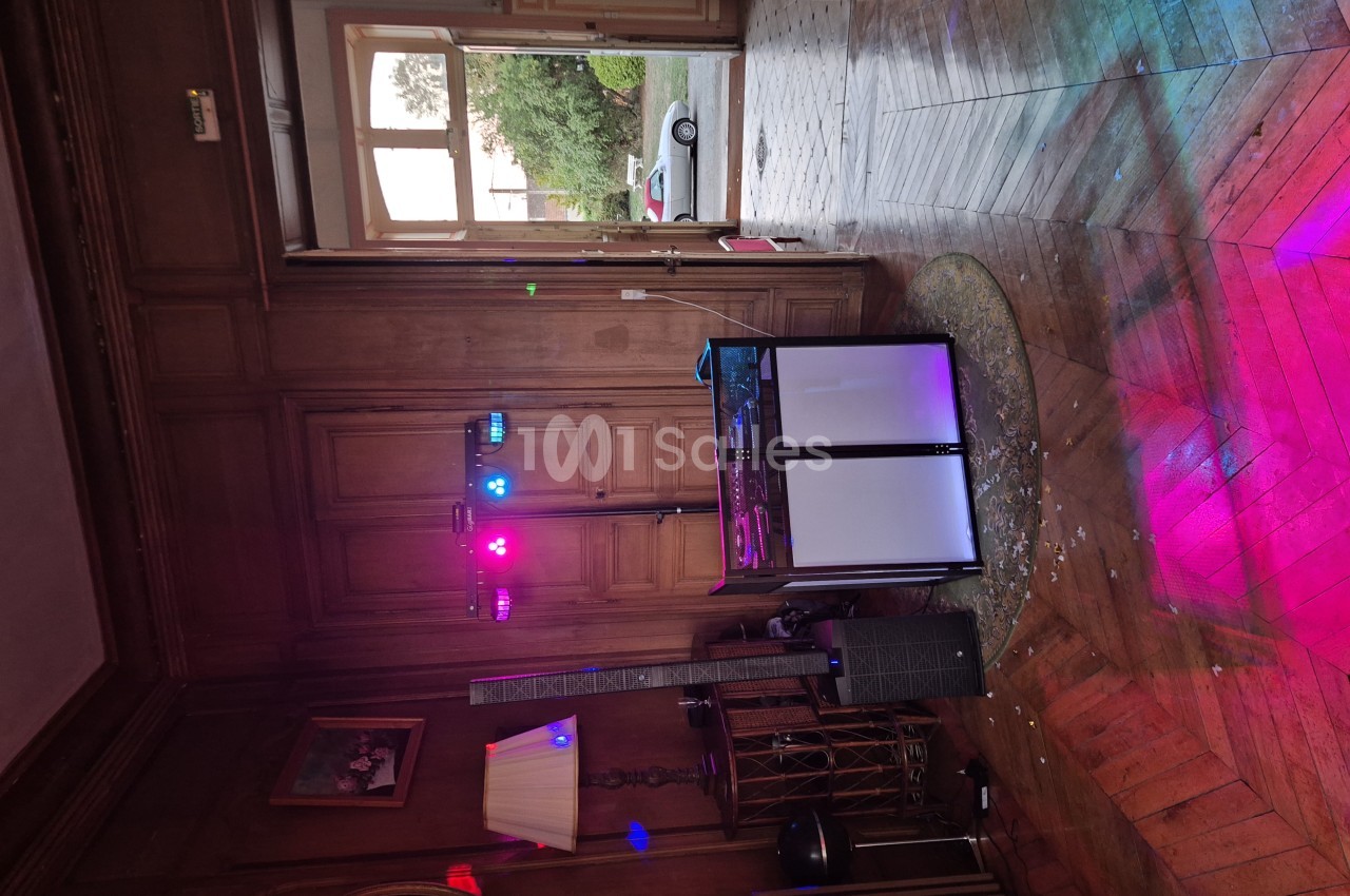 Salle lambrissée au parquet en chevrons éclairé en rose, avec un pupitre de DJ et des projecteurs LED sur pied.