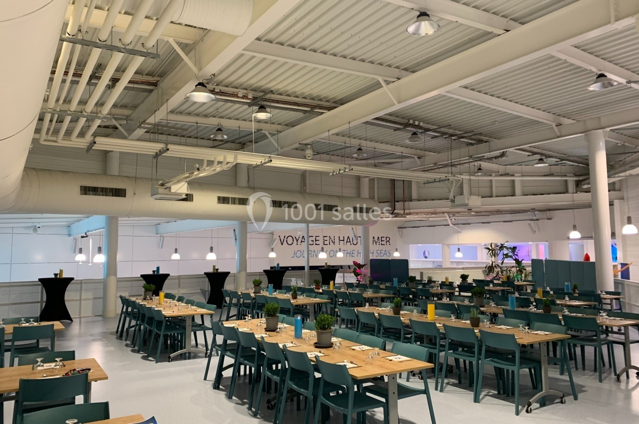 Salle de restaurant lumineuse avec des tables en bois, des chaises vertes et une décoration sobre.