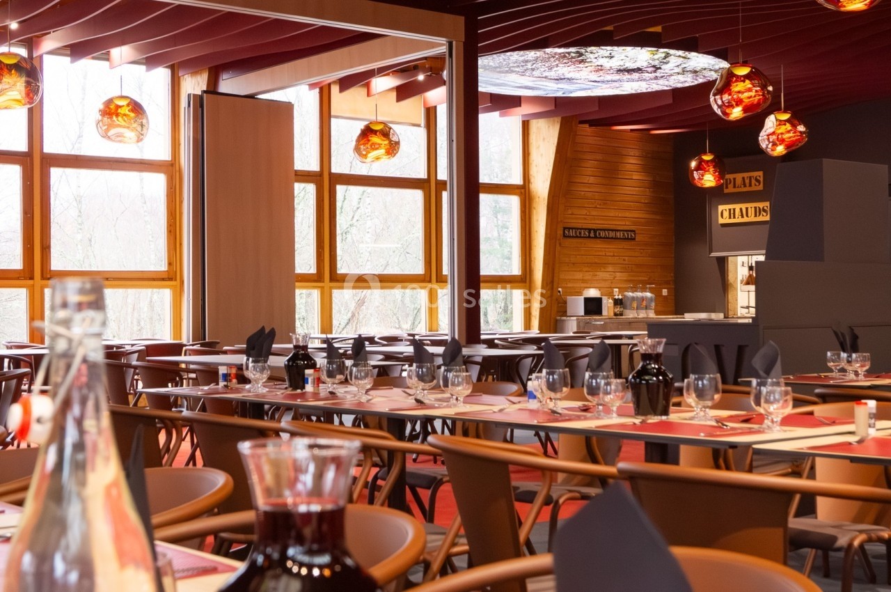 Salle de restaurant lumineuse avec tables dressées, grandes baies vitrées et décorations suspendues colorées.