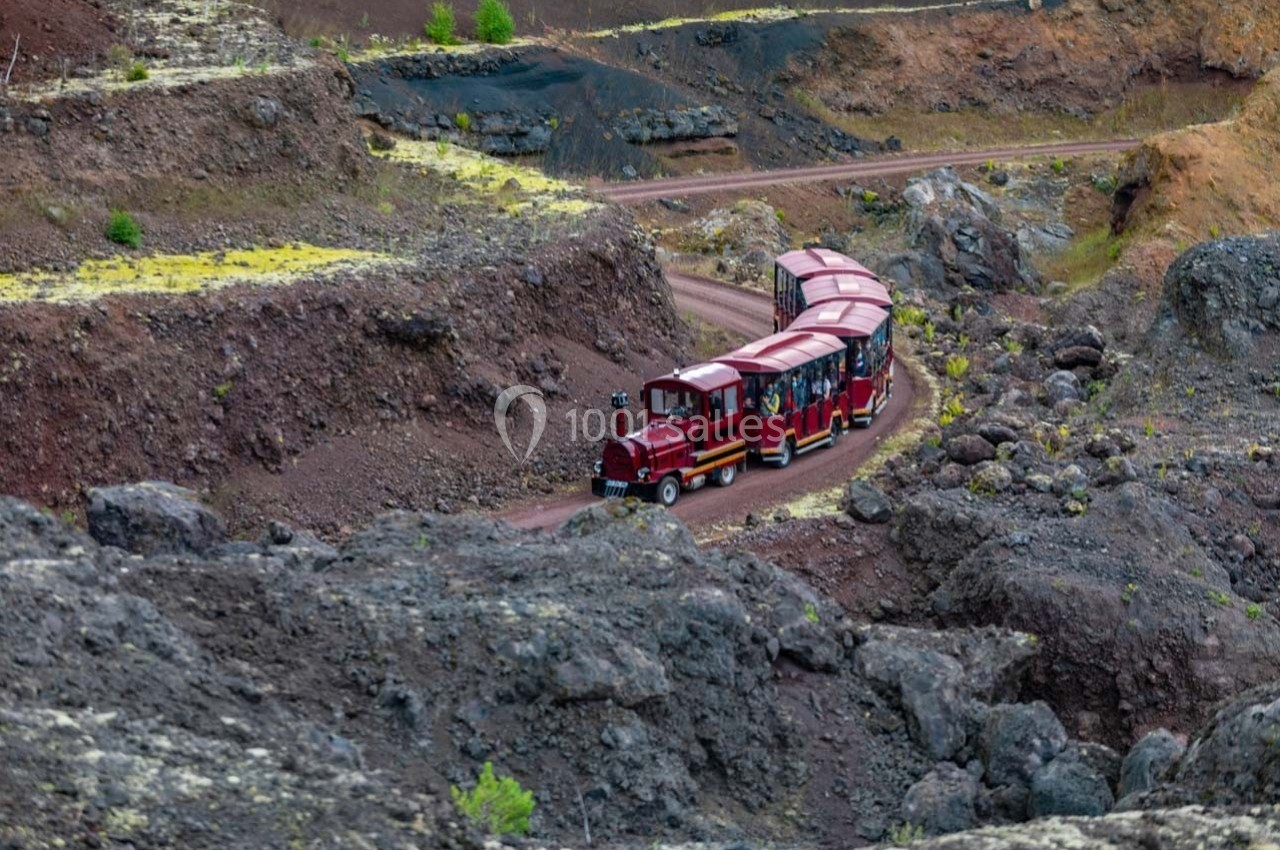 Petit train rouge transportant des passagers sur un chemin sinueux au milieu d'un paysage volcanique rocheux.