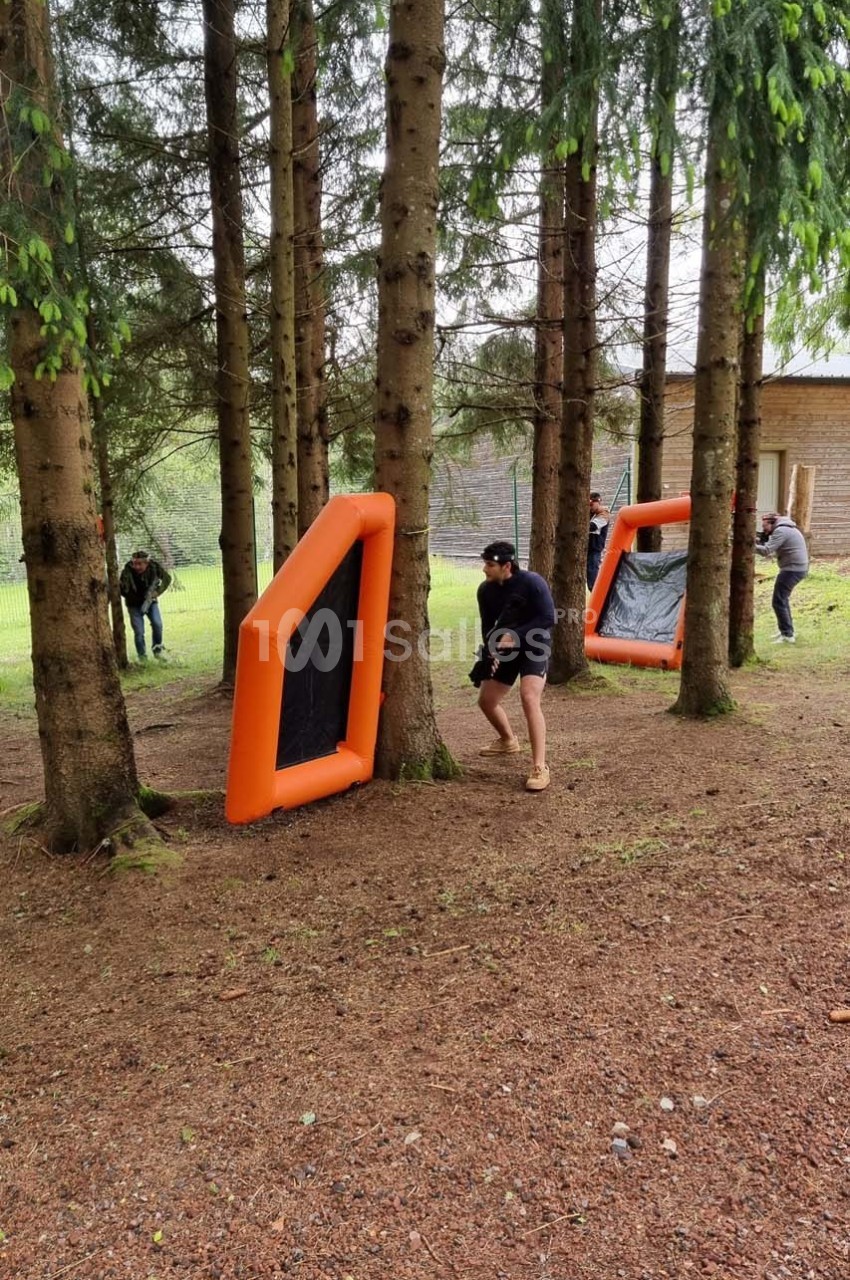 Personnes jouant à un jeu d'extérieur avec des obstacles gonflables orange dans une forêt.