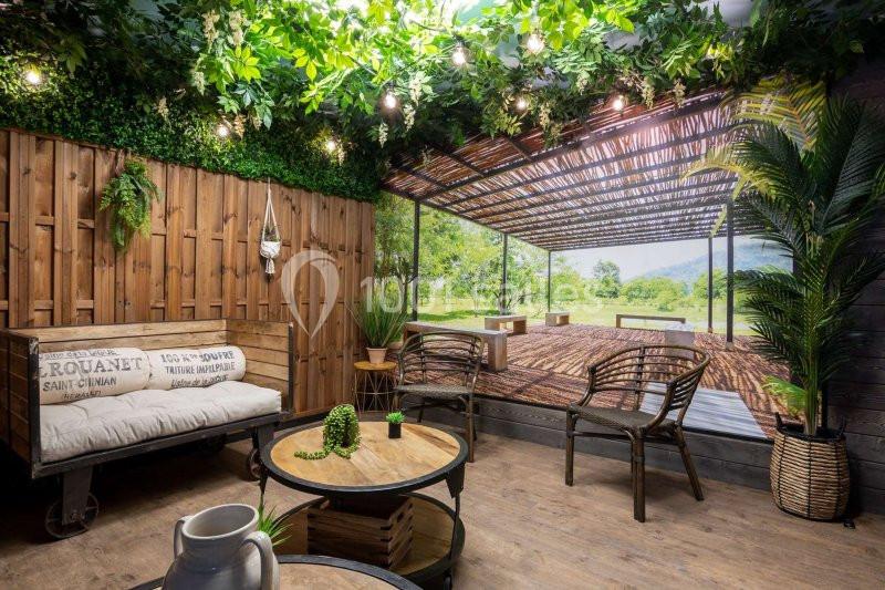 Espace intérieur décoré avec des plantes, des meubles en bois et une fresque représentant une terrasse ouverte sur la nature.