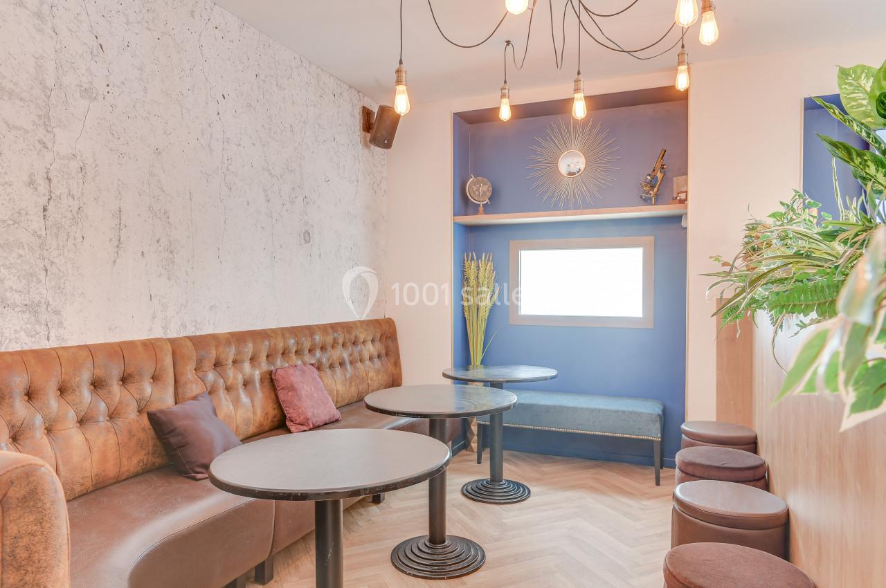 Espace salon avec banquette en cuir, tables rondes, mur bleu décoré et luminaires suspendus.