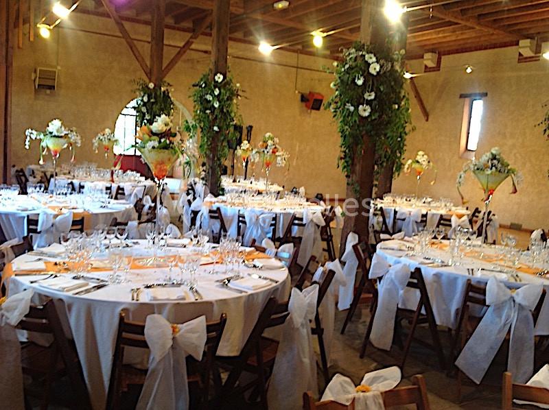 Salle de réception décorée pour un événement, avec tables rondes dressées, nappes blanches et compositions florales.