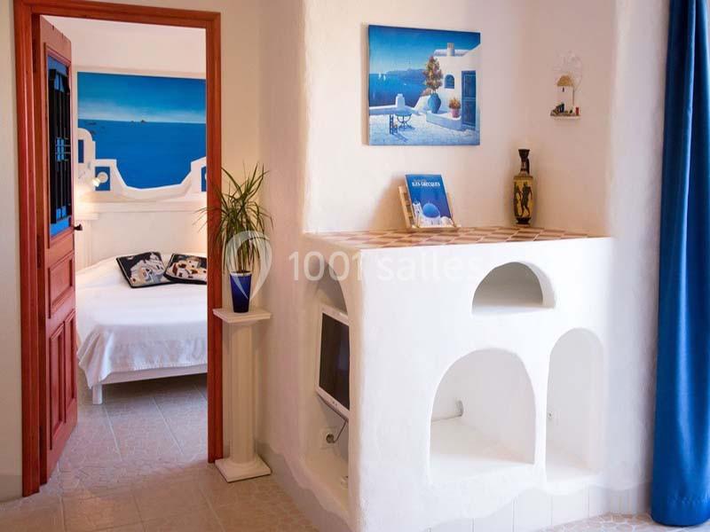 Intérieur lumineux de style méditerranéen avec alcôves blanches, décoration marine et vue sur une chambre adjacente.