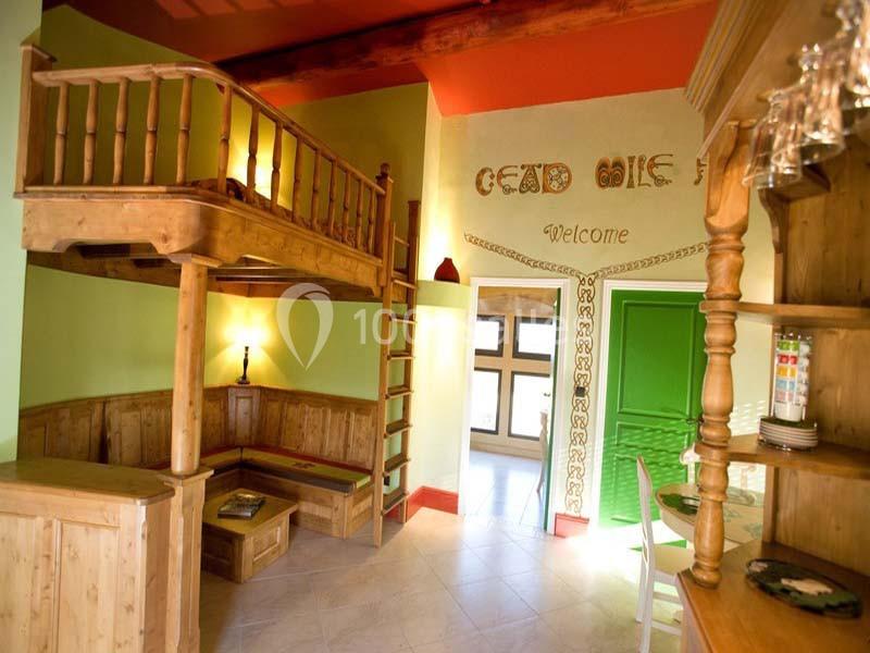 Intérieur lumineux avec mezzanine en bois, mobilier rustique, mur vert et décoration murale accueillante.