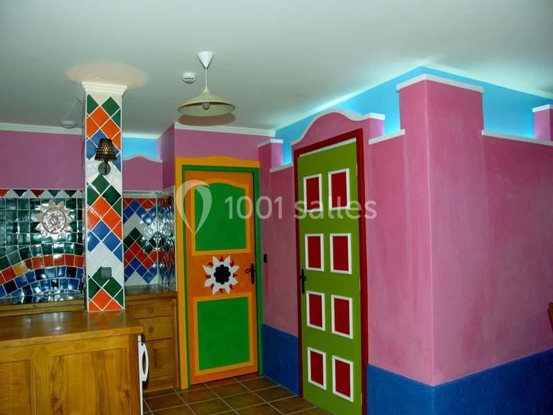 Mur intérieur coloré avec des portes vives, mosaïques décoratives et meubles en bois dans une pièce lumineuse.