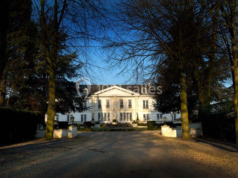 Allée bordée d'arbres menant à une grande maison blanche de style classique sous un ciel dégagé.