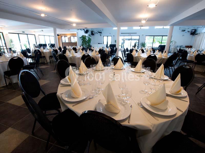 Salle de réception avec tables rondes dressées, nappes blanches, serviettes pliées et vaisselle élégante.