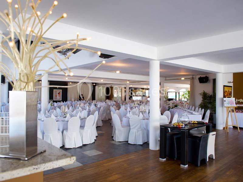 Salle de réception lumineuse avec tables rondes dressées, chaises blanches et décoration moderne.