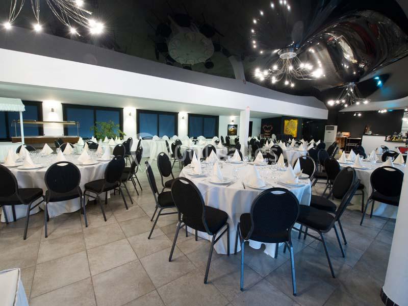 Salle de réception avec tables rondes dressées de nappes blanches, chaises noires et éclairage moderne.