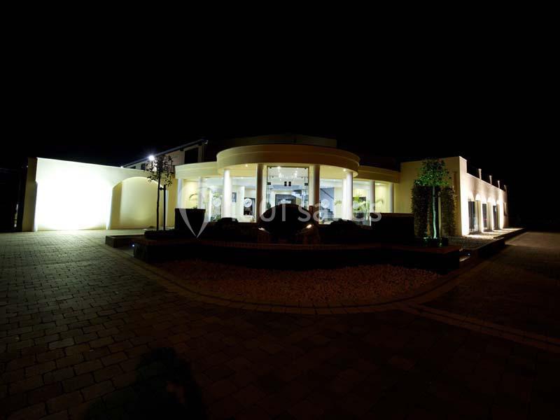 Bâtiment moderne éclairé la nuit, avec une entrée vitrée et des éclairages mettant en valeur l'architecture.