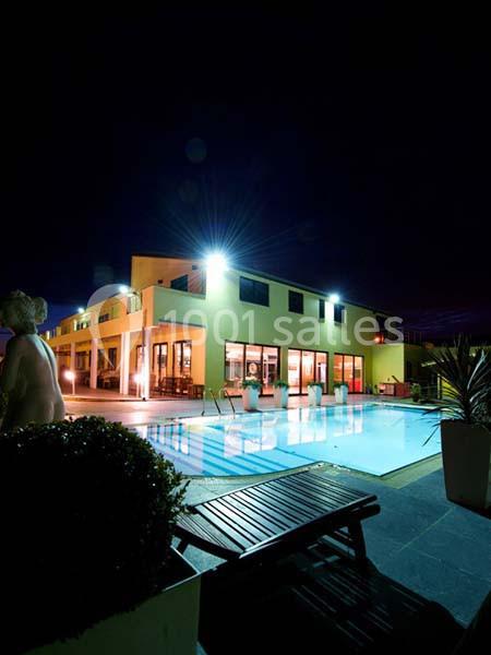 Vue nocturne d'une piscine éclairée devant un bâtiment moderne avec baies vitrées et mobilier extérieur.