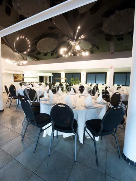 Salle de réception avec tables rondes dressées, nappes blanches, serviettes pliées et chaises noires.