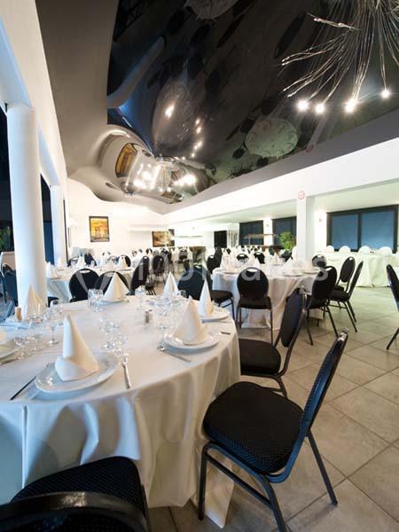 Salle de réception élégante avec tables rondes dressées, nappes blanches et chaises noires, éclairage moderne.