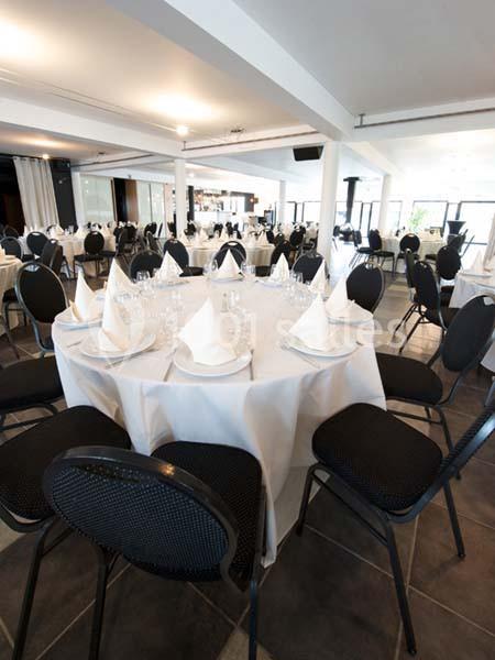 Salle de réception avec tables rondes dressées de nappes blanches, serviettes pliées et chaises noires.