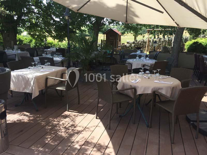 Terrasse ombragée avec tables dressées, chaises en osier et parasols, entourée de verdure et d'arbres.
