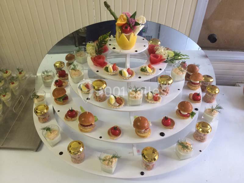 Présentoir circulaire avec verrines, mini-burgers, bouchées et décoration florale au sommet.