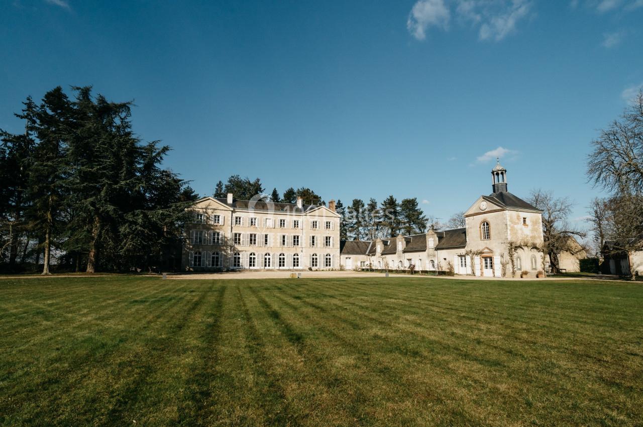 Bâtiment historique entouré d'arbres avec une pelouse bien entretenue sous un ciel bleu clair.
