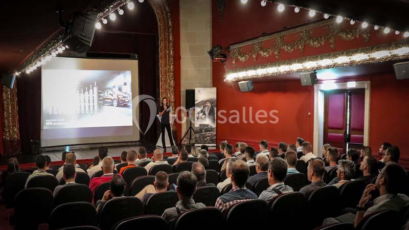 Une conférencière présente un graphique sur un écran devant un public assis dans une salle de théâtre.